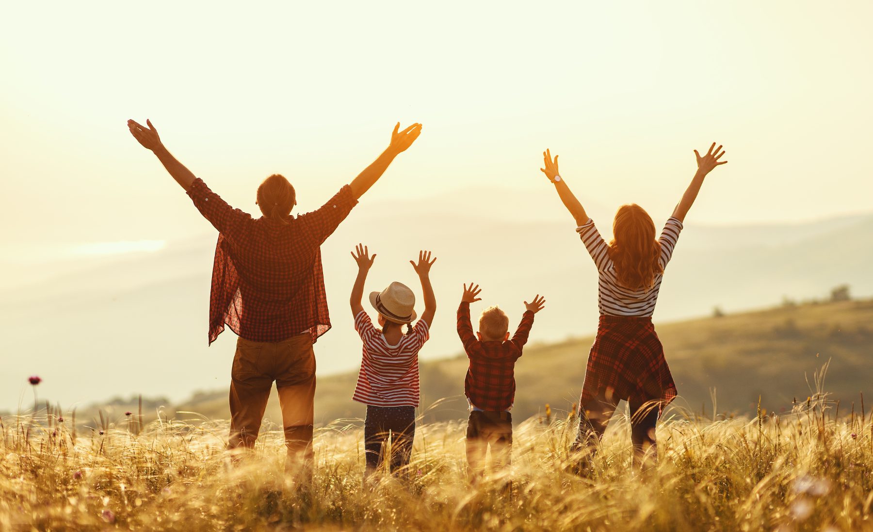 Familie mit erhobenen Armen bei Sonnenuntergang